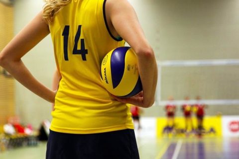 Female volleyball player holding ball, looking away, view of their torso.