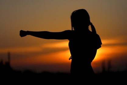 Lady in front of setting sun with fist out in protective pose