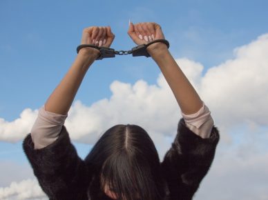 Girl handcuffed with arms above head, looking down