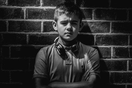 Tween leaning against brick wall, unhappy