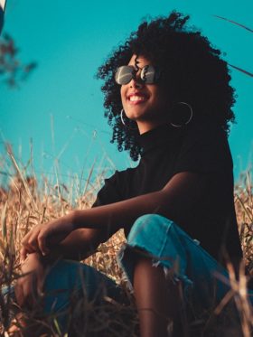 African American girl sitting with sunglasses in field