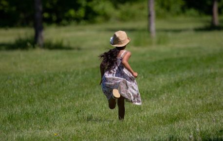 Girl running away with straw hat on in grass