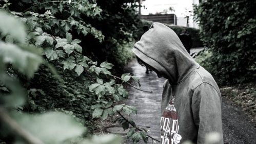 Student with grey hoodie, looking down next to plants