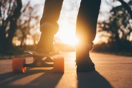 One foot on a skateboard, sun shining between feet.