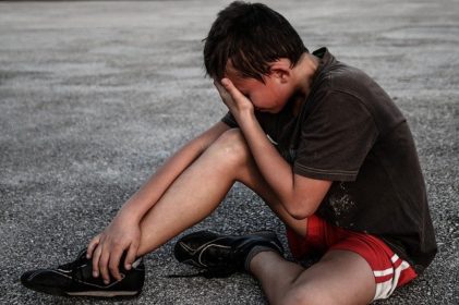 Boy crying sitting on ground from side