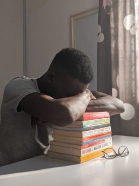 Black student sad with head on top of stack of school books