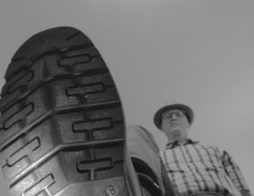 Big bottom of a shoe stepping on something- man with hat in background
