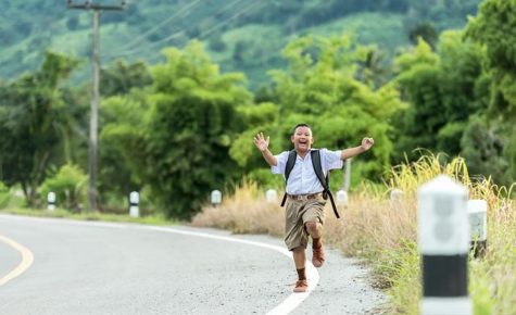 Student running toward camera with backpack along road