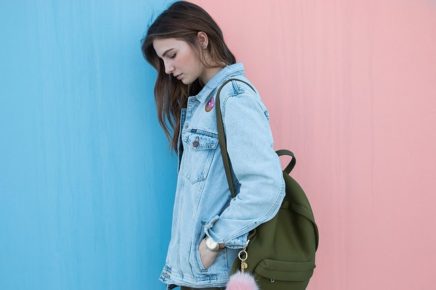 Student with backpack against blue and pink wall, female, looking down