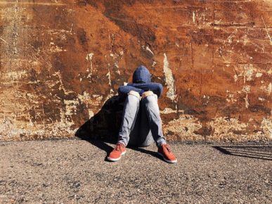 Youth with hoodie on, sitting with head on knees