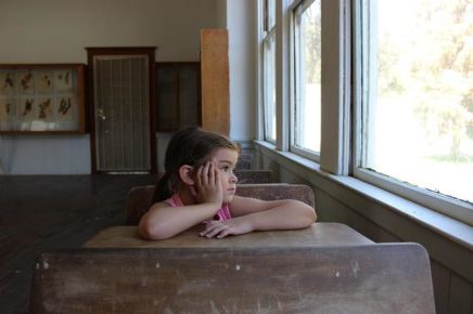 Female student at desk looking sadly outside window