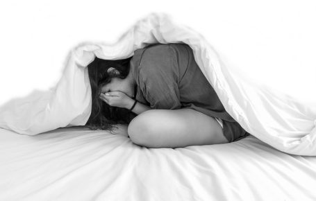 Girl under blanket with hands over face, side view