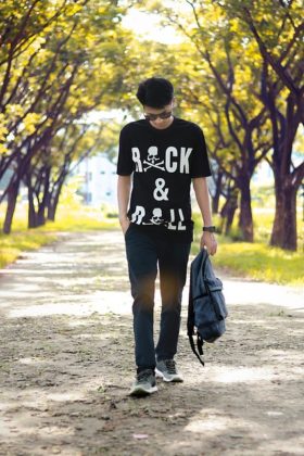 Asian male student walking with head down and backpack in left hand