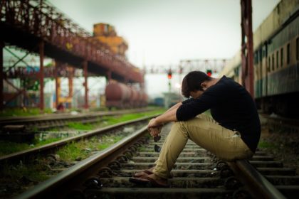 Male student on train tracks with head down
