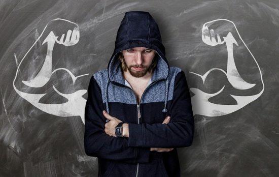 Man leaning against chalkboard with arm muscles drawn behind him