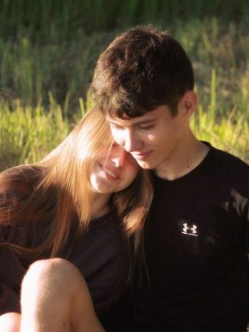 Male and female teen with female leaning on males right shoulder, in field