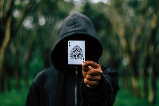 Man with ace card floating in front of face hidden in dark hood