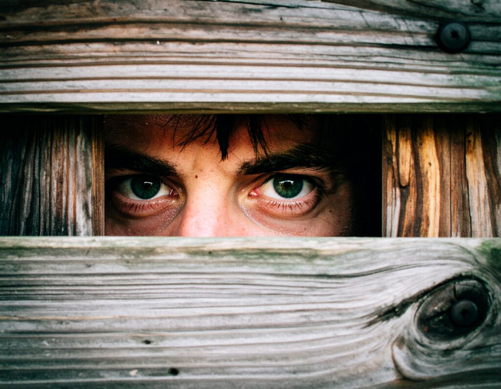 Male student trapped in wooden box, only green eyes peer out