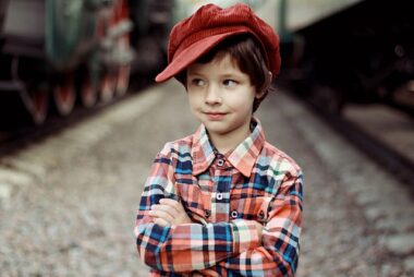Boy in hat looking sideways in plaid shirt, on road