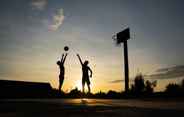 Two kids playing basketball at sunset